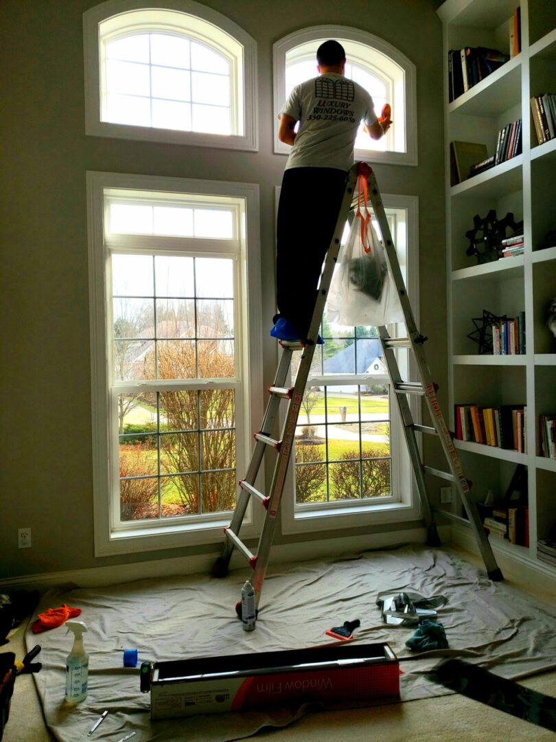 Man on ladder cleaning large interior windows.