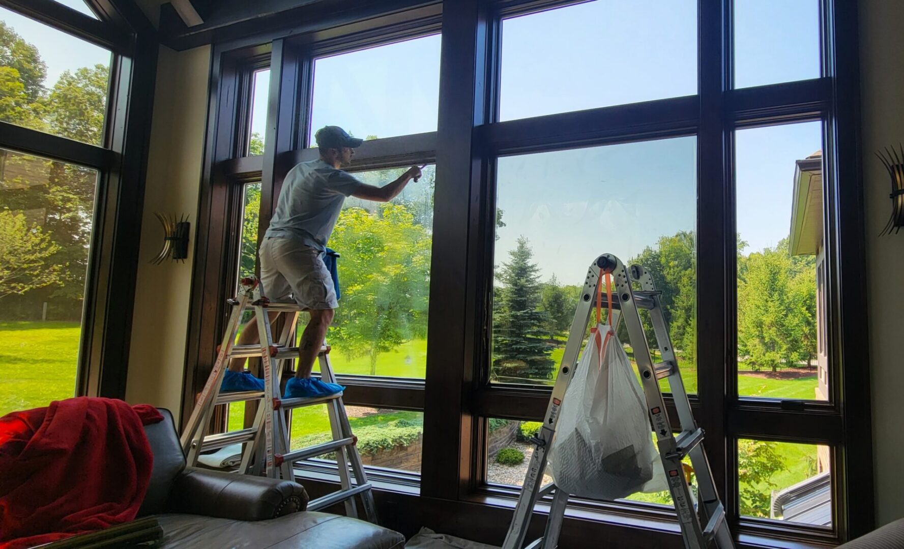 Person cleaning large indoor windows with ladder.
