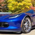 Blue sports car parked near autumn trees.